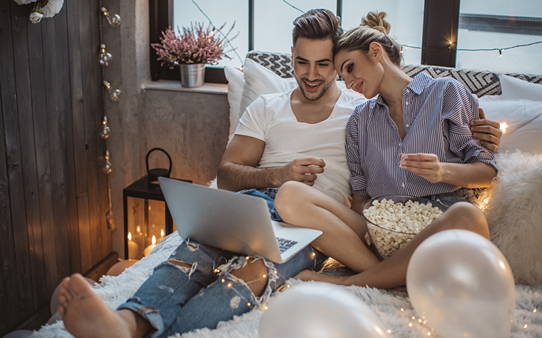 A couple enjoying a movie in bed with popcorn and string lights